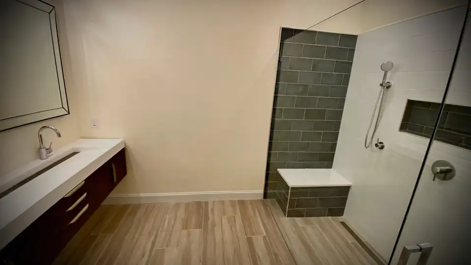 Bathroom remodeling Lake Worth contractor's work: walk-in shower with frameless glass, gray tile accent wall and built-in bench beside a floating dark wood vanity