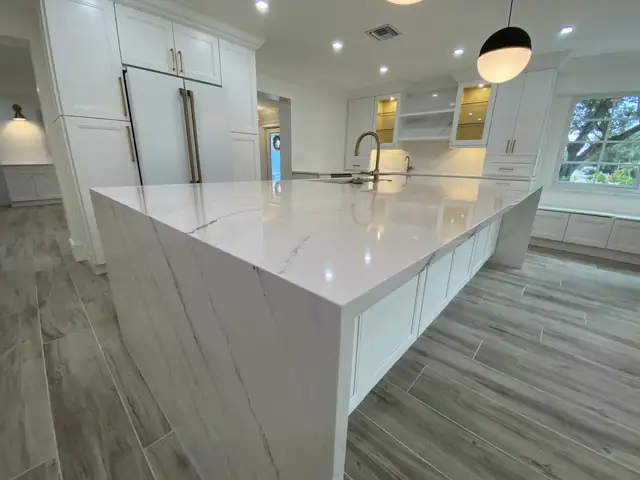 Marble-look quartz waterfall island edge with white cabinetry, a globe pendant and lit glass-front uppers