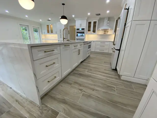 Kitchen island with brushed gold drawer pulls and a quartz top running toward built-in wall ovens